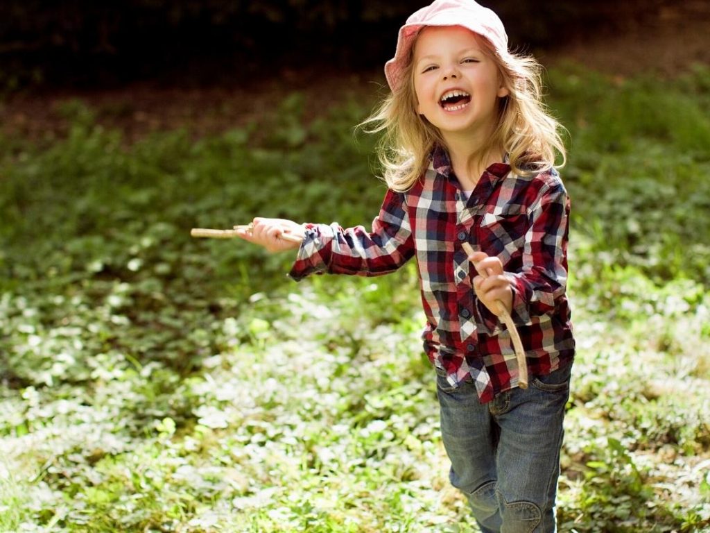 Young girl holds two sticks while smiling
